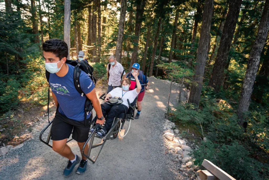 person pulling another person in a wheelchair on an outdoor trail in the woods